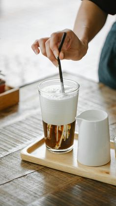 a person is stirring something in a cup on a tray with two cups next to it