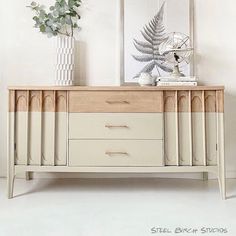 a white and beige dresser sitting next to a plant in a vase on top of a table