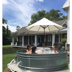 two women sitting in a hot tub with an umbrella over the top and another woman standing next to it