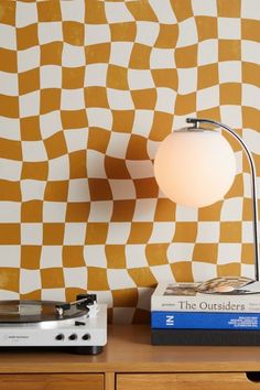 a record player sitting on top of a wooden table next to a wall with an orange and white checkered design