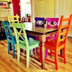 a dining room table with four chairs painted different colors and the floor is made of wood