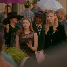 two women standing next to each other in front of a group of people with umbrellas