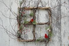 two red birds are perched on branches in front of a white wall with an old window frame