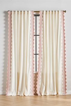 pink and white curtains with scalloped edges in front of a wooden flooring