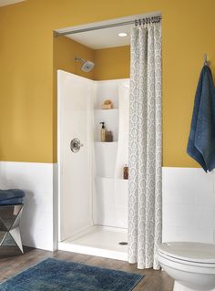 a white toilet sitting next to a shower in a bathroom under a blue rug on top of a wooden floor