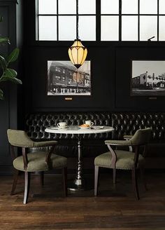 a dining room with black walls and leather boothes, two green chairs at the table