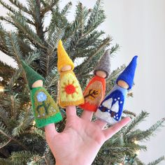 hand holding three small felt gnomes in front of a christmas tree