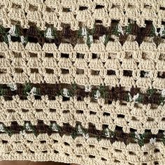 a crocheted blanket with green and brown stripes on it, sitting on a wooden surface