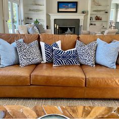 a brown leather couch with blue and white pillows on it in front of a fireplace