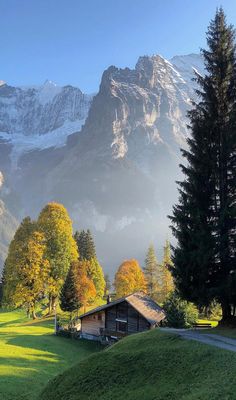 the mountains are covered in snow and green grass, with a small cabin at the bottom