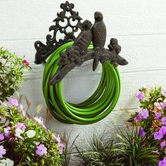 two birds sitting on top of green hoses in front of some plants and flowers