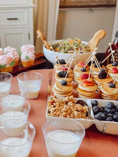 a table topped with lots of desserts and cups filled with milk on top of it