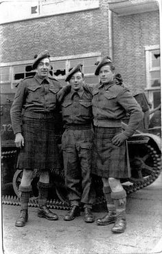 an old black and white photo of three men in uniform standing next to a tank