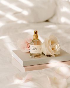 a bottle of perfume sitting on top of a bed next to a white rose flower