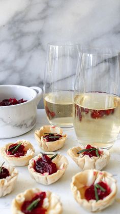 several small pies with cranberry sauce on them next to two glasses of wine