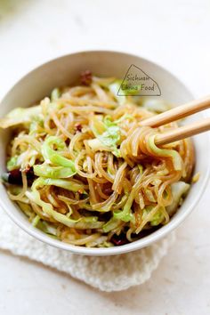 a bowl filled with noodles and vegetables on top of a white cloth next to chopsticks