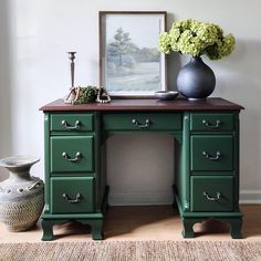 a green desk with drawers and a vase on the top, in front of a white wall