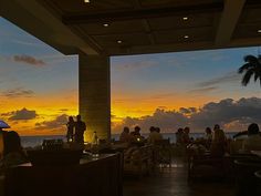 people are sitting at tables on the beach watching the sun go down in the distance