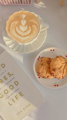 two cookies on a plate next to a cup of coffee and a copy of god's good life