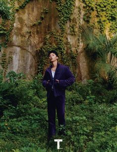 a man standing in front of a wall covered in vines and plants with his eyes closed