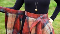 a woman wearing a plaid skirt and black top with a necklace on her left hand