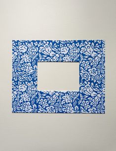 a blue and white square frame with flowers on the border is hanging on a wall