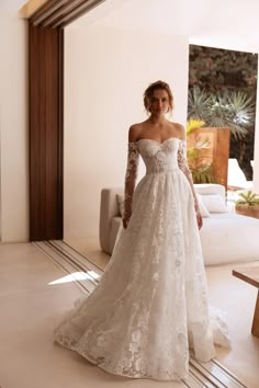 a woman in a white wedding dress standing on the floor with her arms behind her back