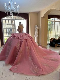 a pink ball gown is displayed in front of a large window with a chandelier