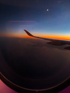 the wing of an airplane as it flies over the ocean and land at sunset or sunrise