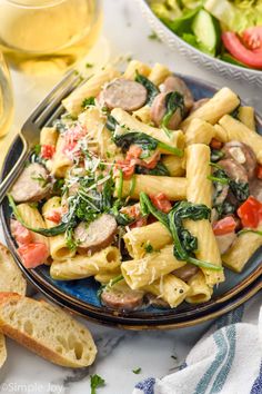 pasta with sausage, spinach and tomatoes on a blue plate next to bread slices