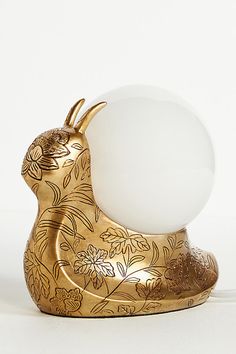 a golden rabbit lamp with an egg in it's mouth on a white background