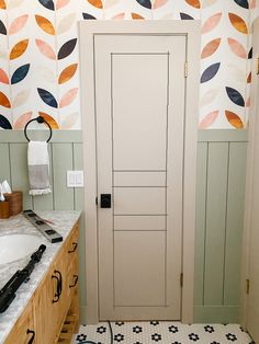 a bathroom with a white door and patterned wallpaper on the walls, along with two sinks