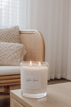 a white candle sitting on top of a wooden table next to a chair and window