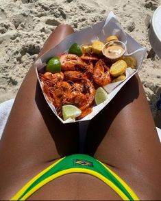 a woman laying on the beach with her legs crossed holding a plate of food