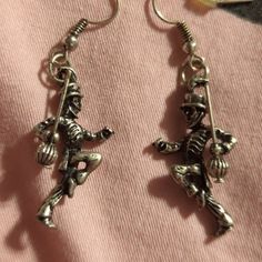 two silver colored earrings with skeleton charms hanging from them on a pink fabric background and a pair of scissors in the foreground