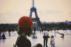 a woman with a red hat standing in front of the eiffel tower, paris