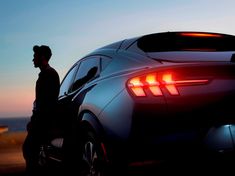 a man standing next to a car with the back lights on at sunset or dawn