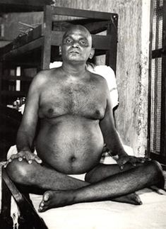 an old man sitting in the middle of a room with his legs crossed and no shirt on