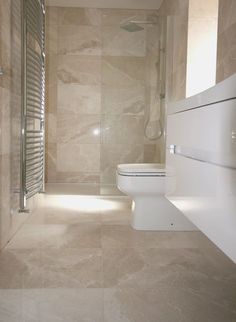 a white toilet sitting in a bathroom next to a walk in shower and tiled walls