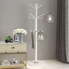 a white coat stand with two lamps on top of it and flowers in vases next to it