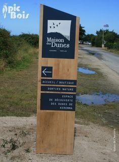 a wooden sign sitting on the side of a road next to a dirt field and grass