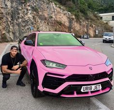 a man kneeling next to a pink sports car