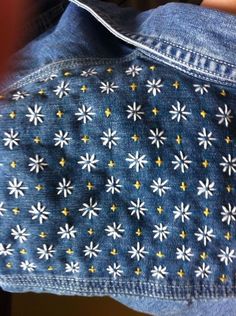 the back of a jean jacket with white and yellow flowers on it, showing buttons