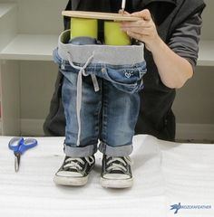 a child is sitting on a table with scissors and pencils in his pocket while holding two yellow cups