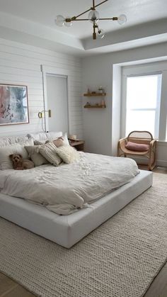 a large bed sitting in the middle of a bedroom next to a window with white walls