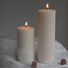 two white candles sitting next to each other on top of a sheet of wax paper