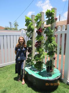 a woman standing next to a garden with plants growing on it's sides in the grass