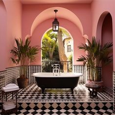 an ornate bathroom with pink walls, black and white tile flooring and a claw foot tub