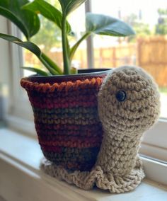 a small crocheted snail sitting on top of a window sill next to a potted plant