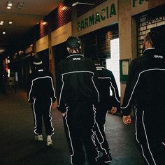 three men walking down the street holding hands and wearing black jackets with white writing on them